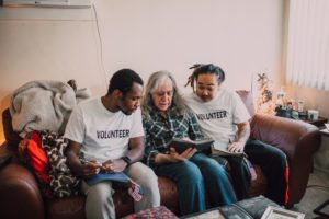 Two volunteers sitting on a couch with an elderly man.